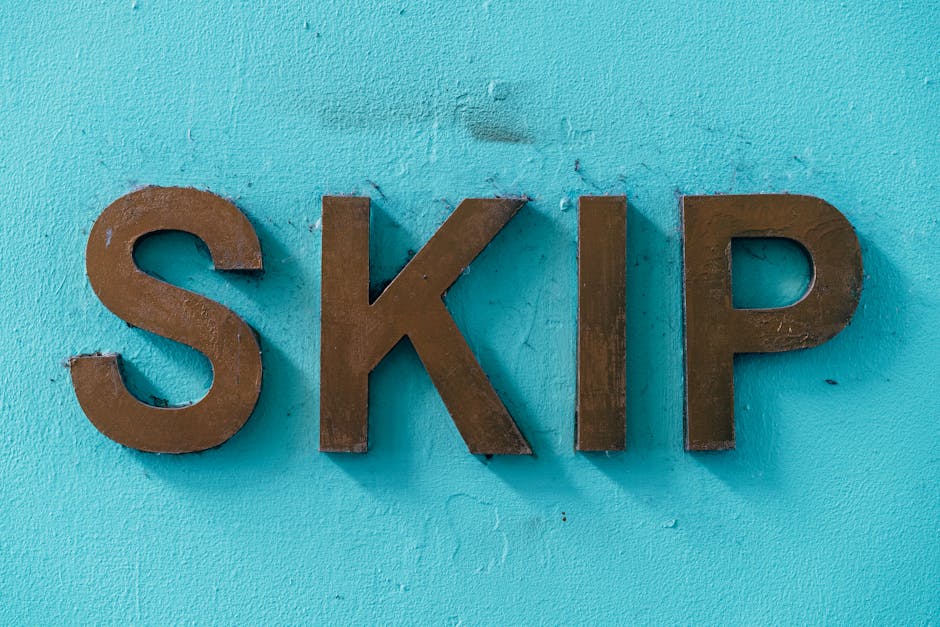 Metal letters spelling 'SKIP' mounted on a light blue wall, with the letters positioned horizontally. The letters are three-dimensional, with a brownish finish, and appear to be made of metal or wood. The wall background is smooth with some visible texture, and there is no other object or signage visible in the image. The photograph is well-lit, highlighting the contrast between the brown letters and the blue wall, providing a clear and detailed view suitable for accessibility and supporting content related to house removals, packing, or moving logistics, such as obtaining a skip permit during a home relocation in Wapping. This setting represents an exterior or interior wall often seen in property or service signage, relevant for moving and transport services like those provided by Man With a Van Wapping.